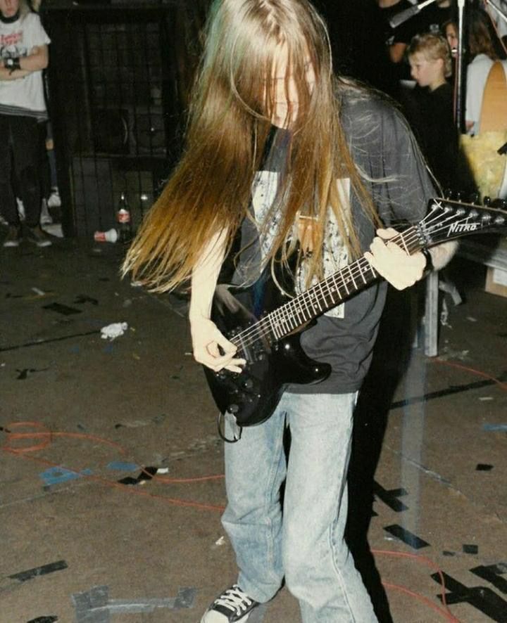 a man with long hair playing an electric guitar in front of a group of people