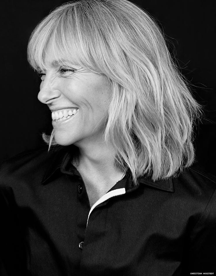 a black and white photo of a woman with blonde hair smiling at the camera while wearing a black shirt