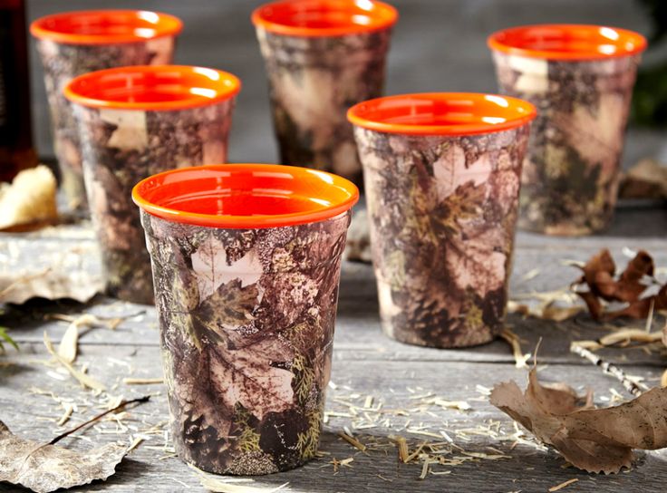 four shot glasses with orange rims sitting on a table next to leaves and a bottle