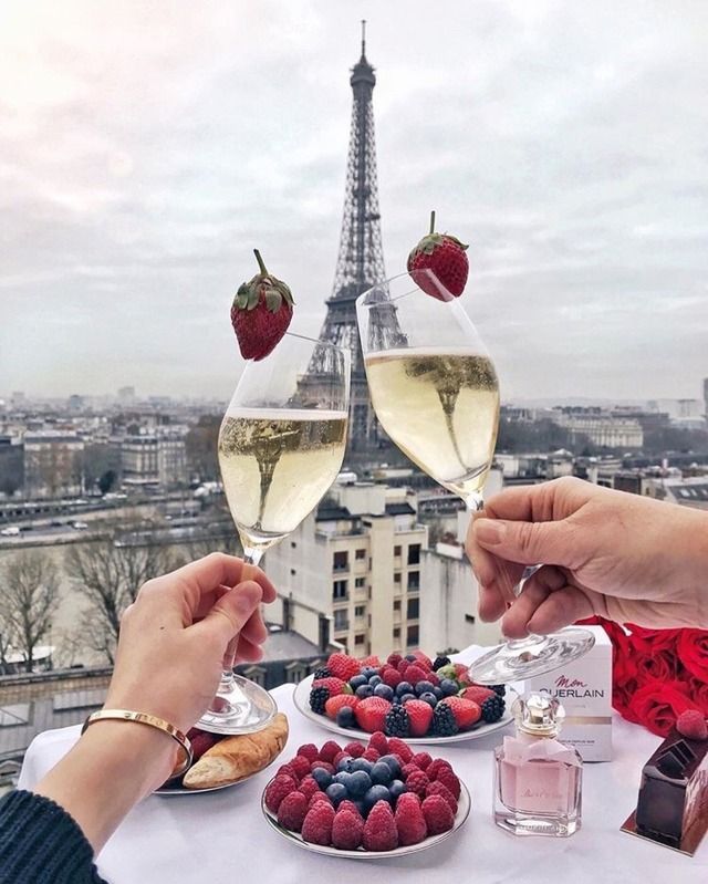 two people toasting glasses of wine and berries on a table with the eiffel tower in the background