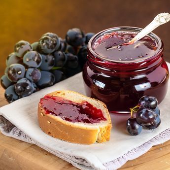 a jar of jam next to bread and grapes