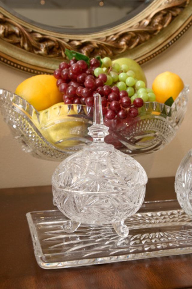 a glass bowl with grapes and lemons in it on a table next to a mirror