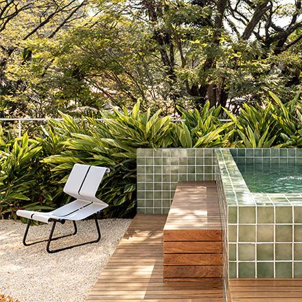 a chair sitting next to a swimming pool in the middle of a lush green forest