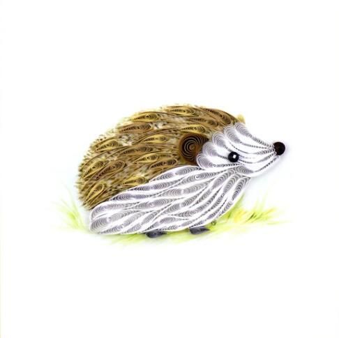 a hedgehog brooch sitting on top of green grass with gold and silver accents