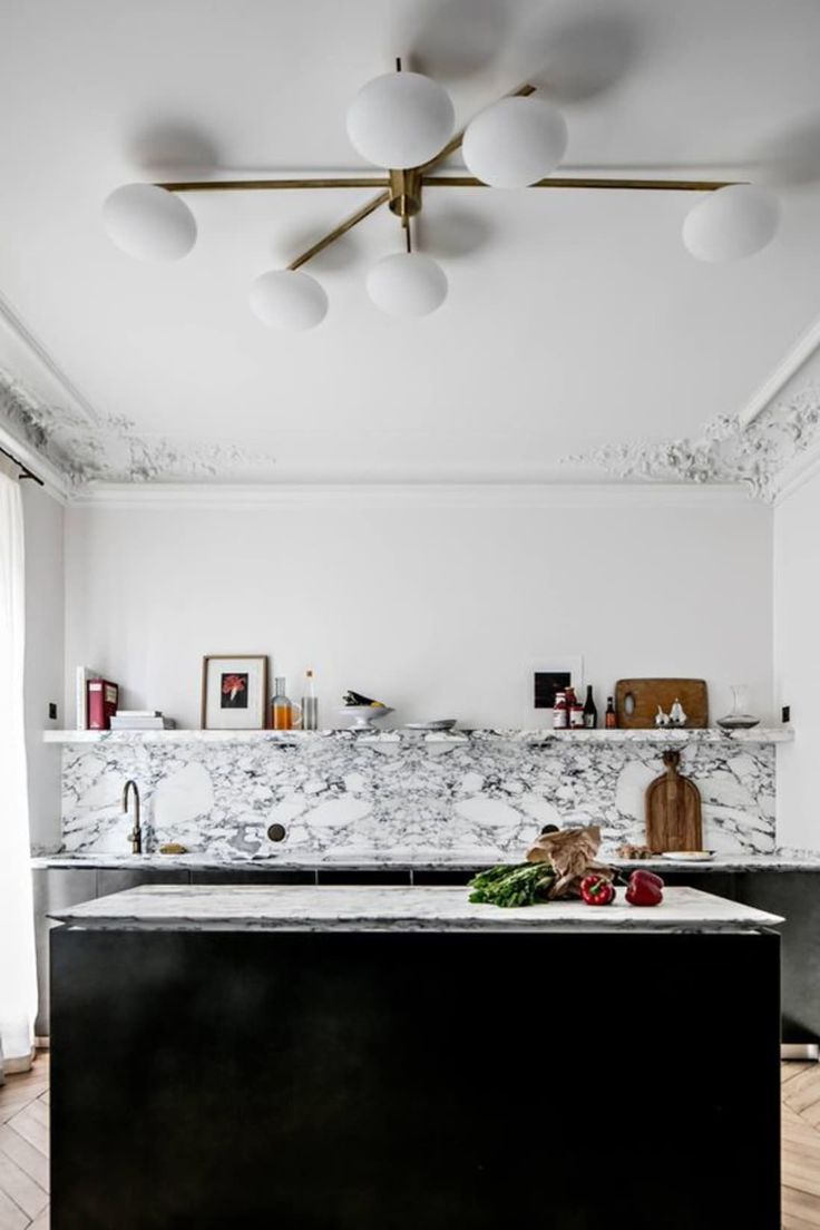 a kitchen with marble counter tops and black appliances in the center, surrounded by white globe lights