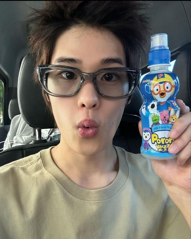 a young man holding up a bottle of water in his hand while sitting in the back seat of a car