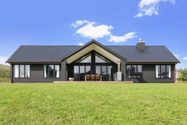 a large house with a black roof and windows on the front lawn, surrounded by lush green grass