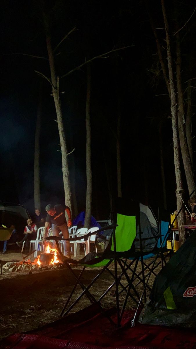 people sitting around a campfire in the woods at night with their tents set up