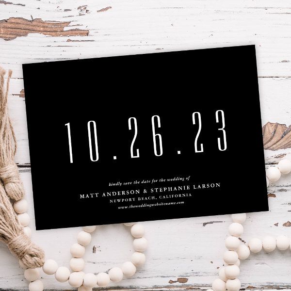 a black and white wedding save the date card with tassels around it on a wooden table