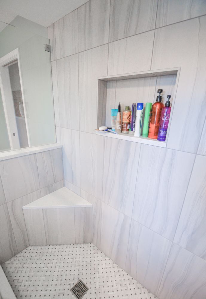 a white tiled bathroom with shelves on the wall and toiletries in the shower area