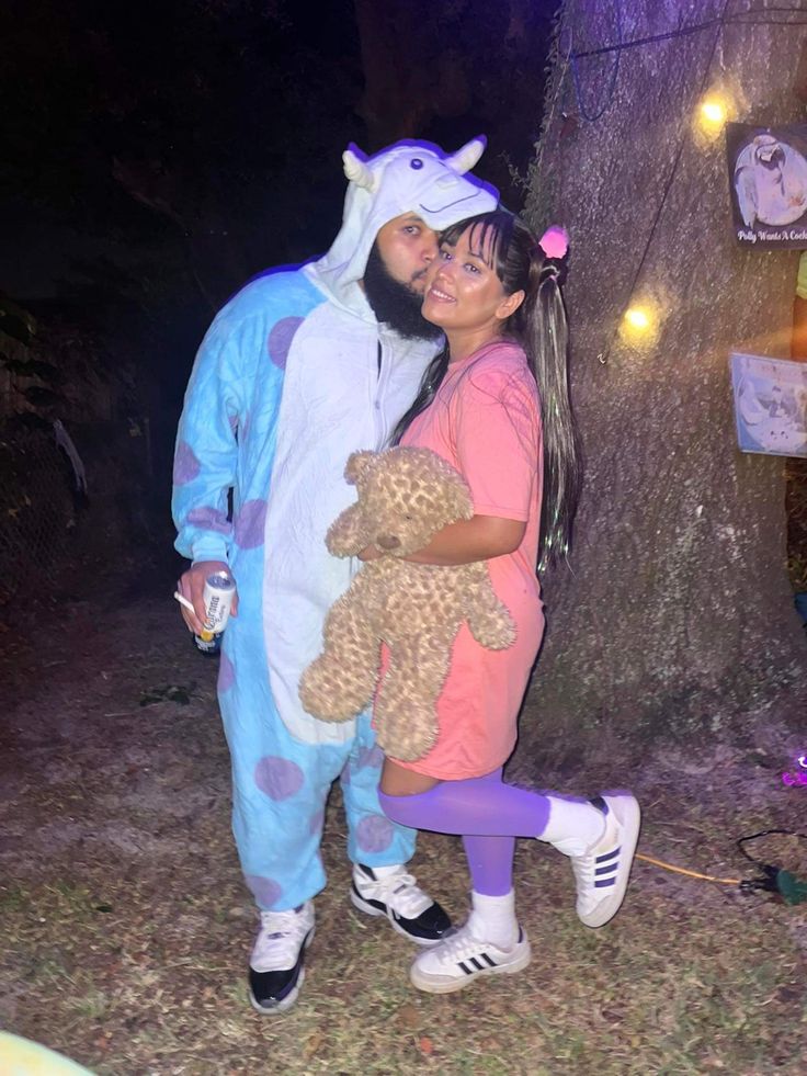 a man and woman dressed up in costumes standing next to a tree with their arms around each other