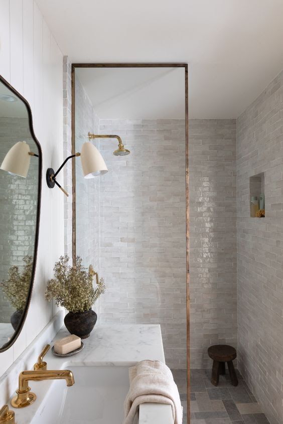 an instagramted photo of a bathroom with white tile and gold fixtures, including a large mirror on the wall