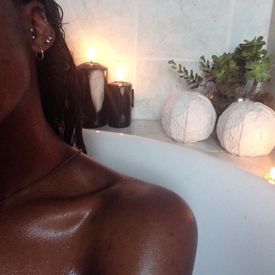 a woman sitting in a bathtub with candles on the wall next to her head