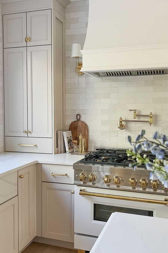 a kitchen with white cabinets and gold pulls on the stove top, along with an oven hood