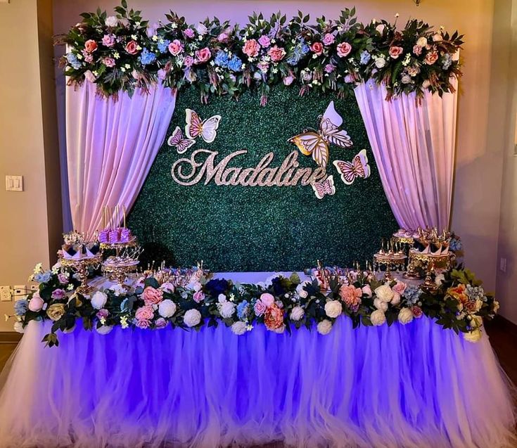 a table topped with flowers and butterflies under a mardi gras sign that reads,