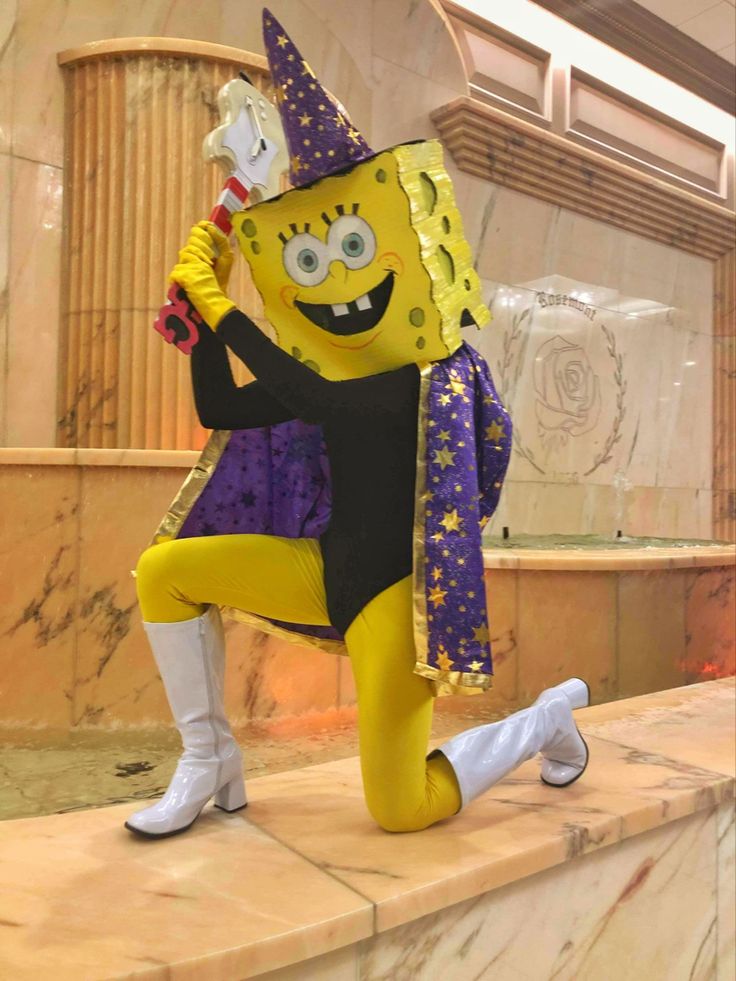 a costumed person sitting on top of a counter in front of a fountain wearing a mask