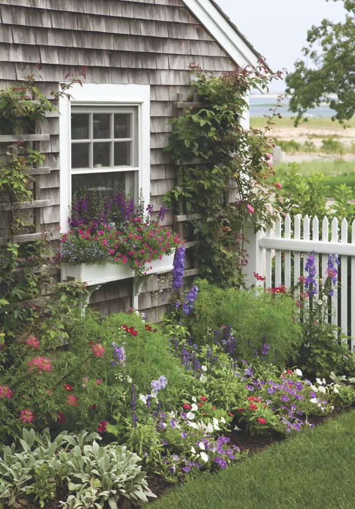 a house with flowers growing on the side of it and a white picket fence in front