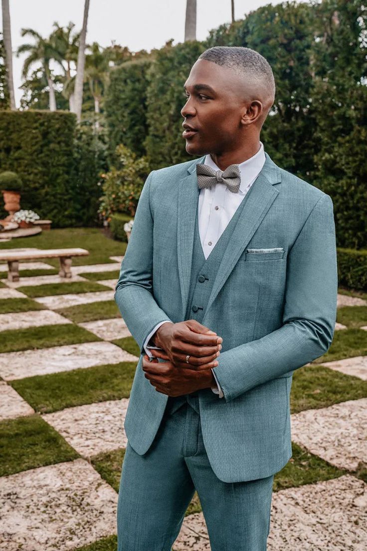 a man in a blue suit and bow tie standing on a checkerboard floor