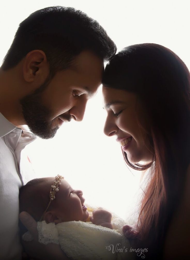 a man and woman holding a baby in their arms while looking at each other's eyes