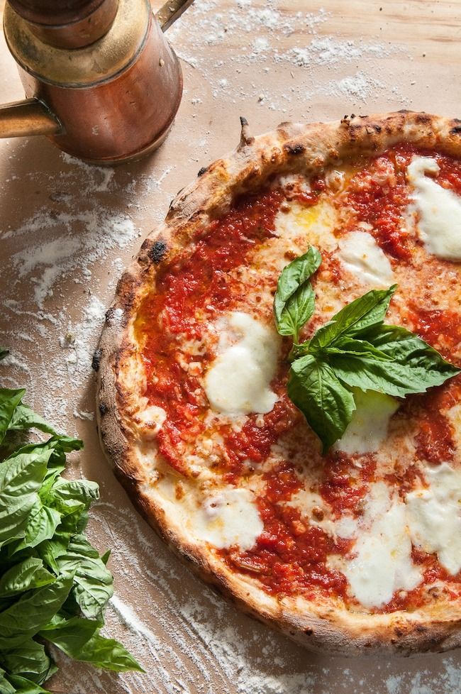 a pizza sitting on top of a wooden cutting board next to basil leaves and a pepper shaker