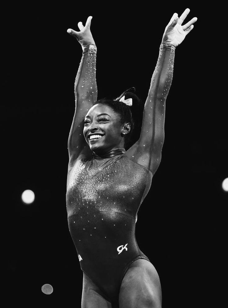 a black and white photo of a woman on the balance beam with her arms in the air