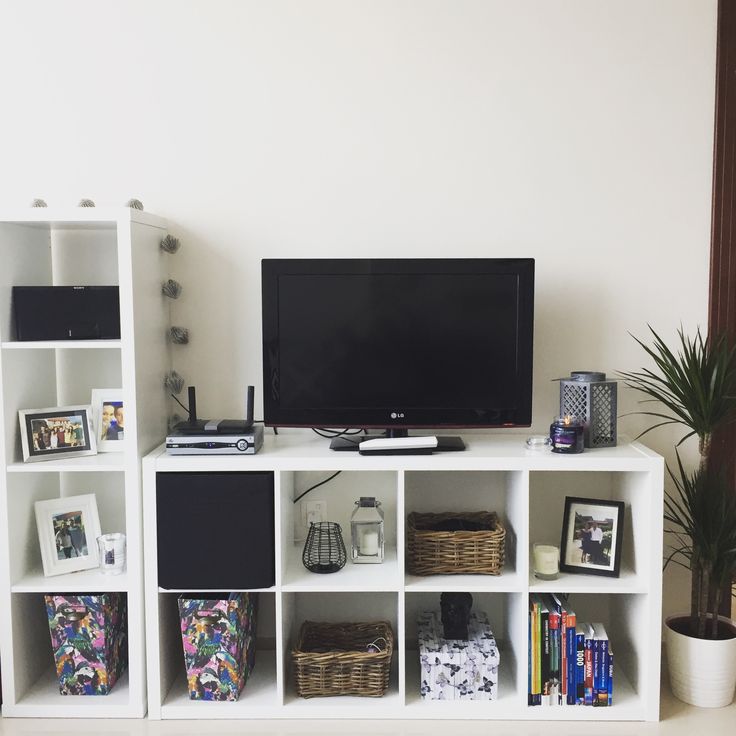 a television is on top of a white shelf with baskets and books in front of it