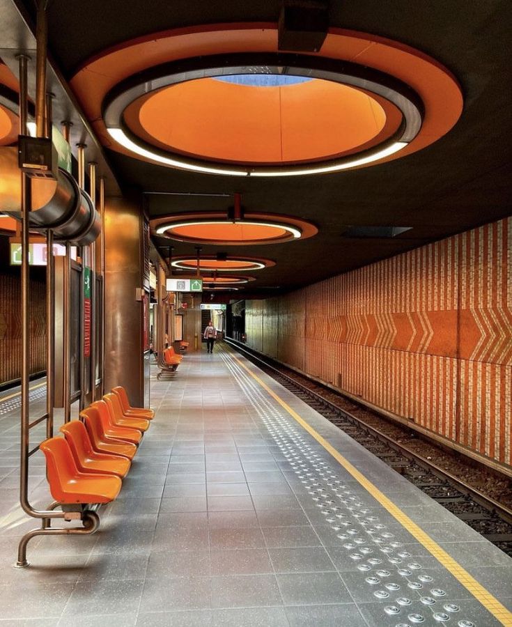 an empty train station with orange chairs and round lights on either side of the platform