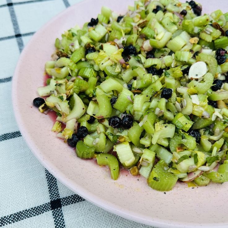 a pink plate topped with celery and blueberries on top of a checkered table cloth