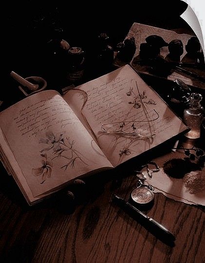 an open book sitting on top of a wooden table next to other writing instruments and objects