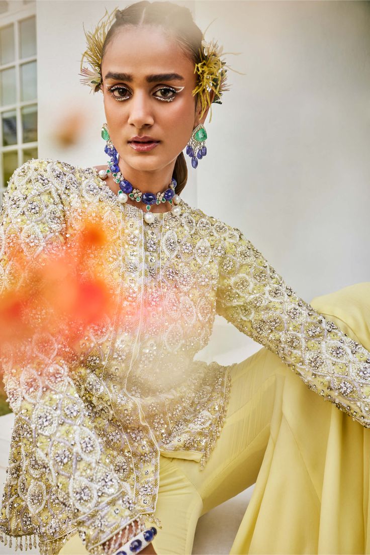 Dazzle in this exquisite set featuring a yellow and lilac jacket adorned with intricate cutdana, pearl, and sequin embroidery, accented by handmade buttons and tassels. Complete the look with chiffon sharara pants and an embroidered net dupatta for a truly regal appearance. Designer Yellow Embellished Kurta, Elegant Long Sleeve Lehenga With Gota Work, Pista Green Embellished Kurta For Festive Occasions, Embellished Pista Green Palazzo Set For Designer Wear, Embellished Pista Green Anarkali Set For Eid, Festive Embellished Pista Green Kurta, Elegant Yellow Palazzo Set With Straight Kurta, Elegant Yellow Palazzo Set With Resham Embroidery, Elegant Yellow Kurta For Navratri