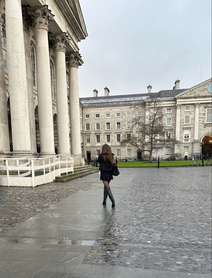 a woman is walking down the street in front of an old building on a rainy day