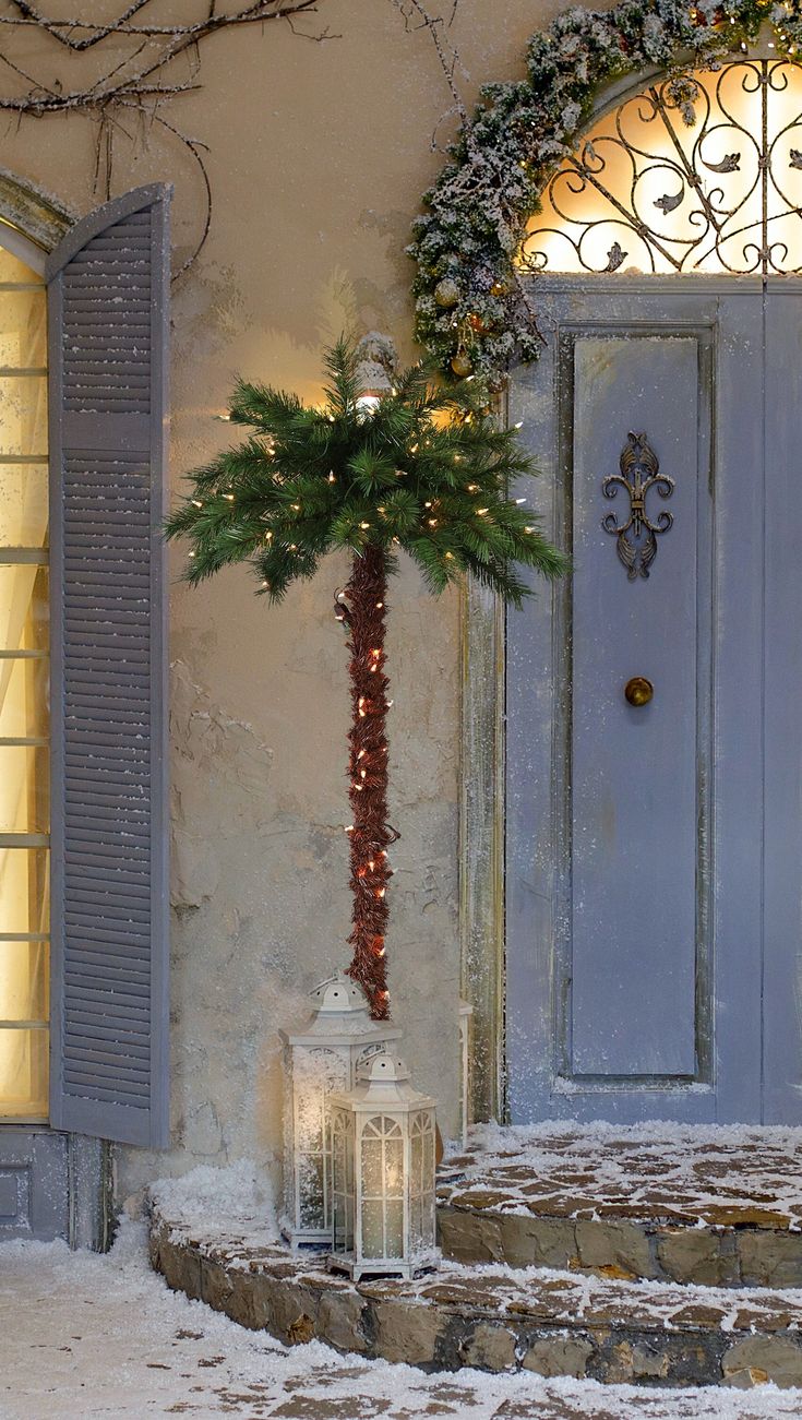 a christmas tree is in front of a blue door with shutters and a lantern