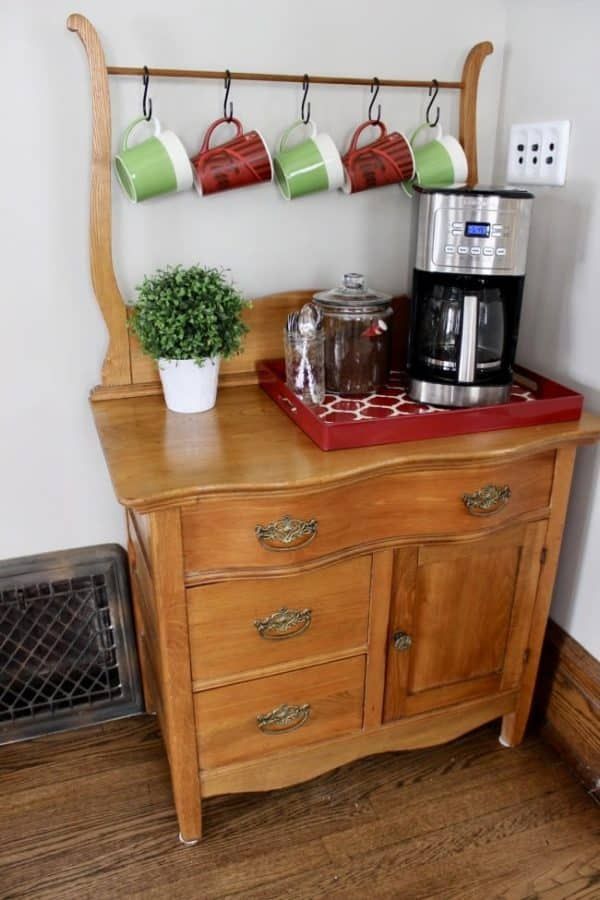 a coffee maker on top of a wooden dresser with cups hanging from it's hooks