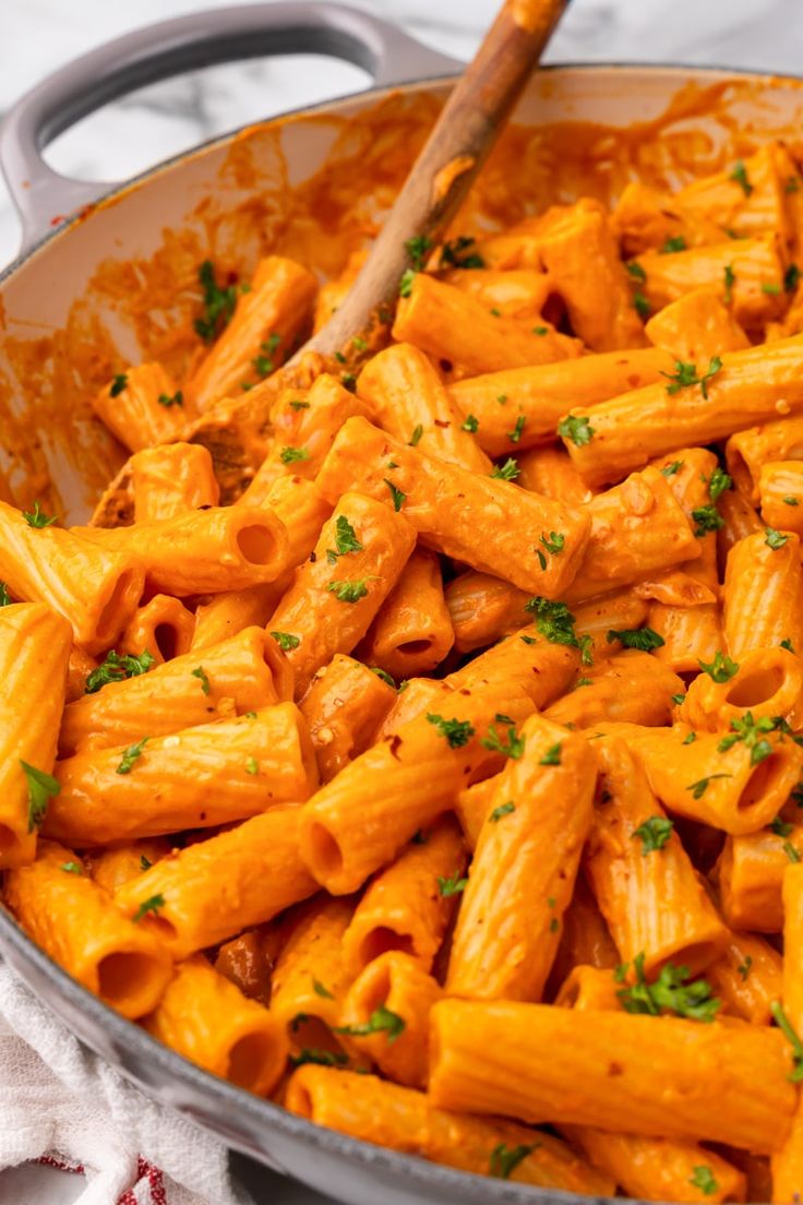 a pan filled with pasta and parsley on top of a white cloth next to a wooden spoon