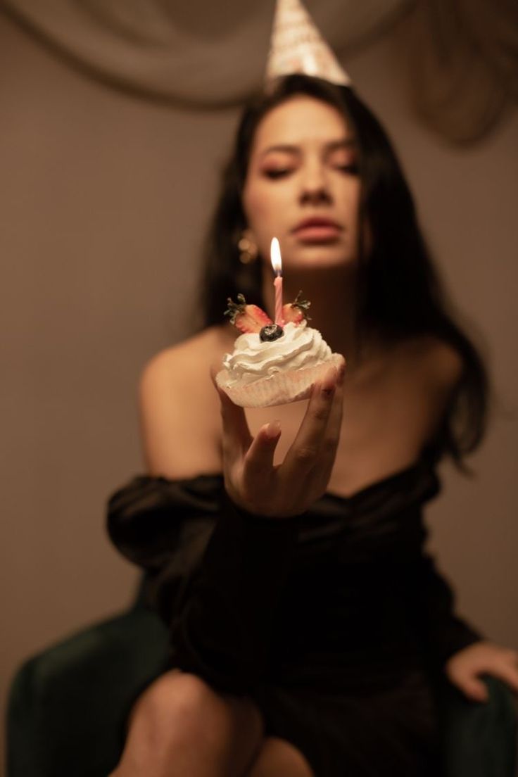 a woman in a black dress holding a cupcake with a candle on it's top