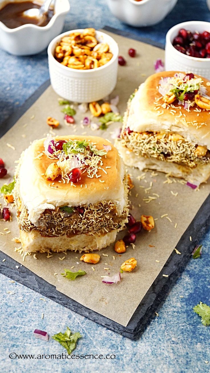 two sandwiches on a cutting board next to bowls of nuts