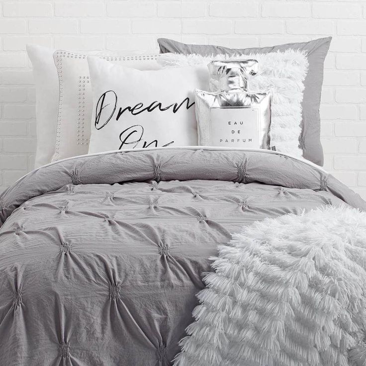 a bed with grey and white comforters on top of it in front of a brick wall