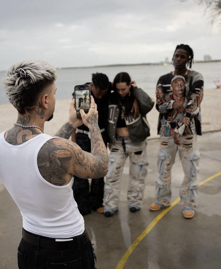 a group of young people taking pictures with their cell phones on the beach while one person takes a picture