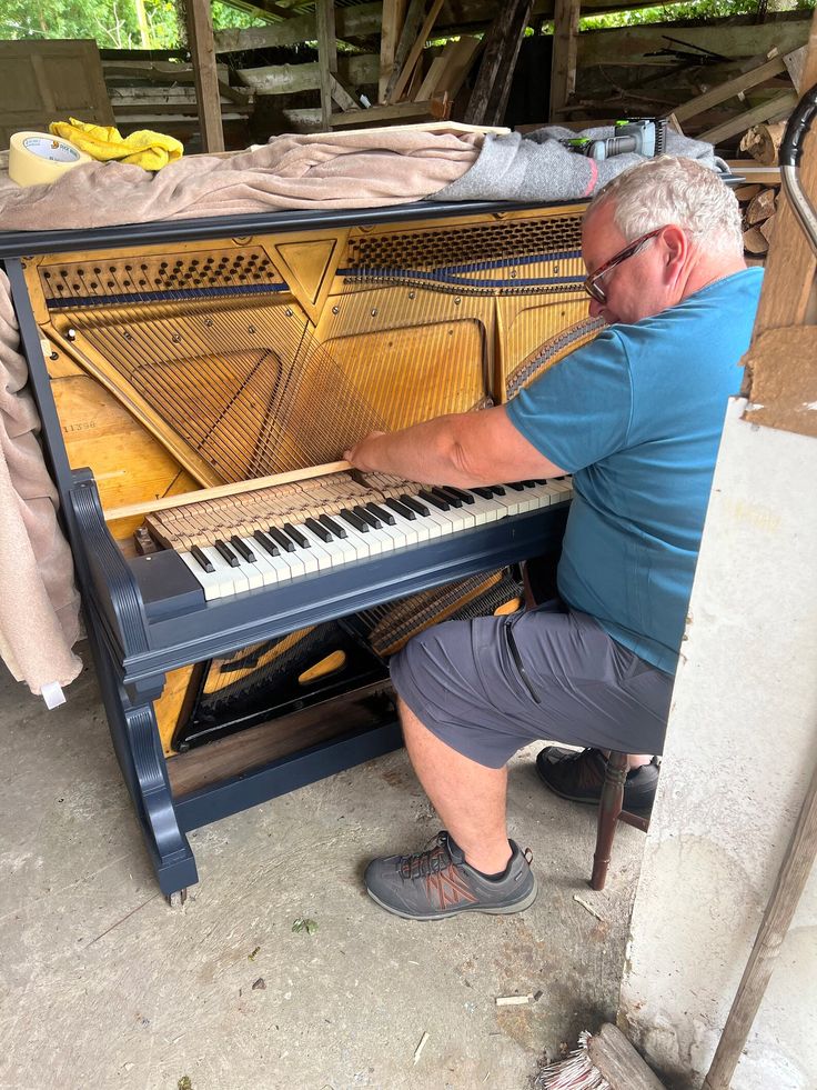 an older man is playing the piano in his garage, while sitting down and looking at it