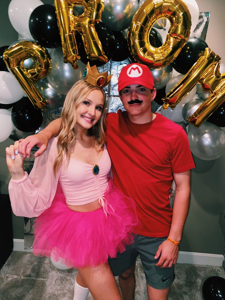 a man standing next to a woman wearing a pink tutu and red hat with balloons behind her