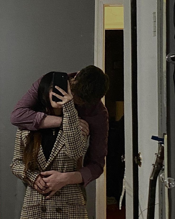 a man and woman embracing each other in front of a door with their arms around each other