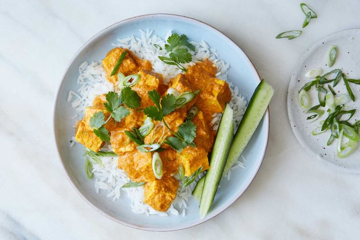 a white plate topped with rice covered in curry and garnished with cilantro