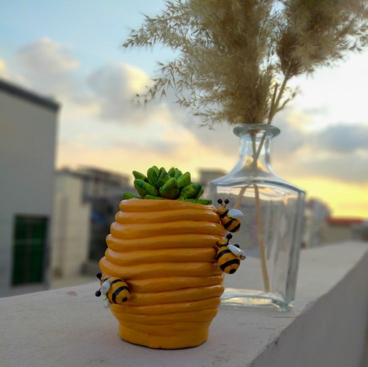 a vase with some plants in it and bees on the outside, near a planter