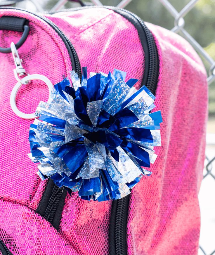 a pink and blue bag with a flower on it's side, sitting next to a chain link fence