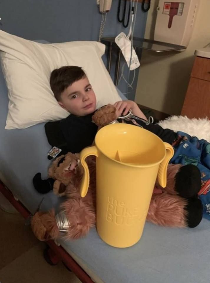 a young boy laying in a hospital bed next to a teddy bear and a cup