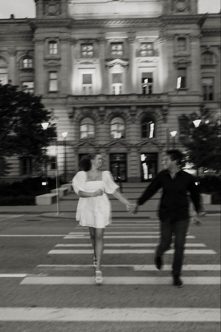 two people walking across a cross walk in front of a building