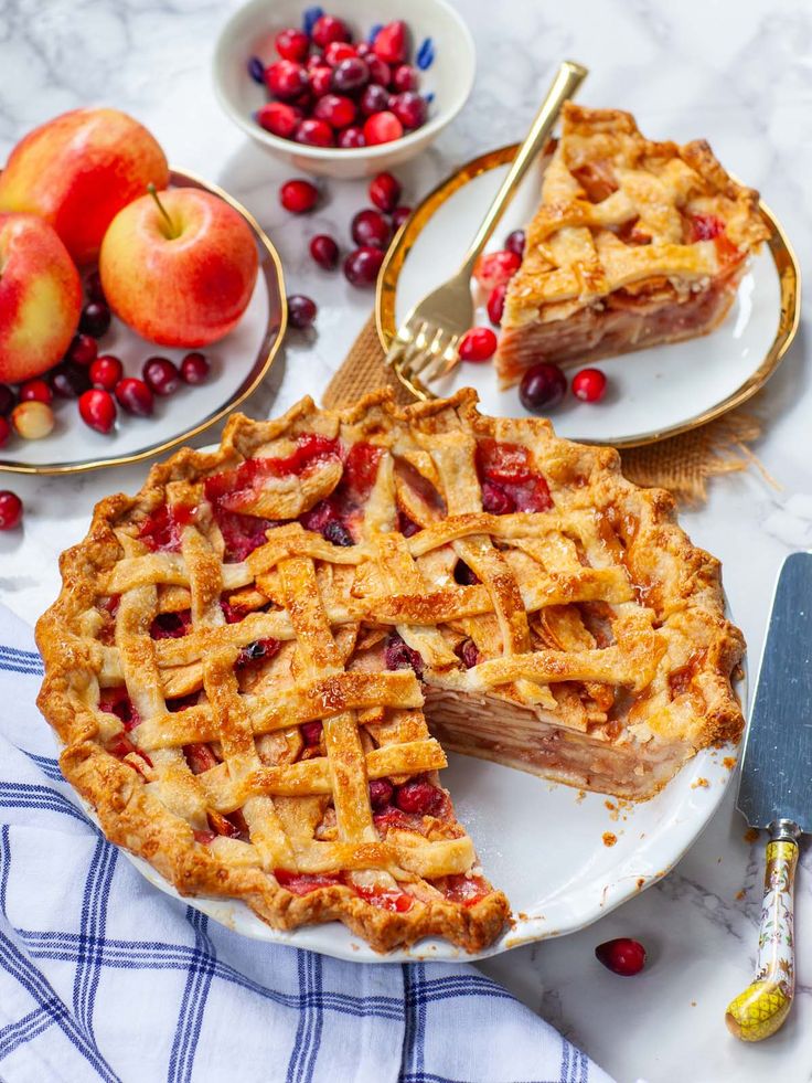 an apple pie is cut into slices on a plate with cranberries and apples in the background