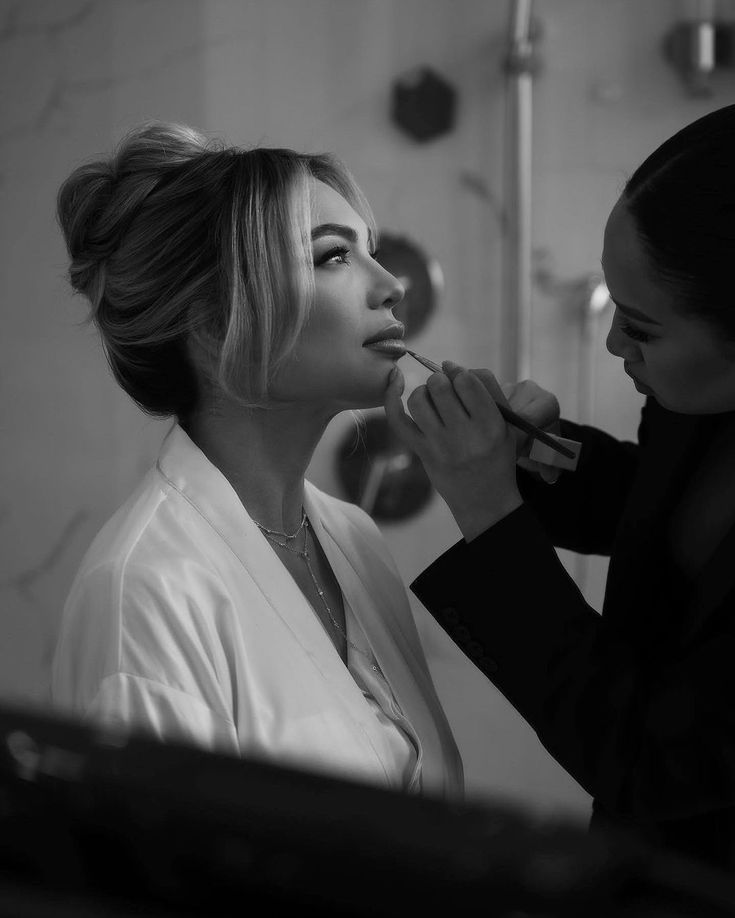 a woman is getting her makeup done by another woman in the bathroom, while wearing a robe