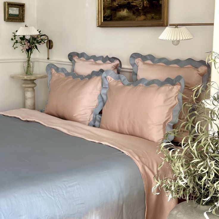 a bed with pink and blue comforters in a white room next to a potted plant