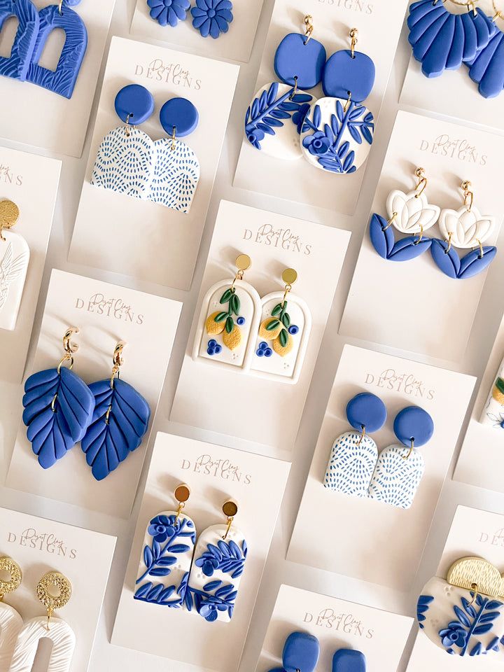 blue and white earrings are on display in front of cards with gold earring designs